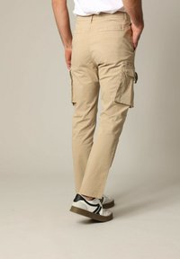 Beige cargobroek met zijzakken, met een rechte pijp en gemaakt van katoen. Draagt bij witte sneakers met zwarte accenten.