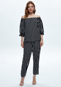 Sort og hvid stribet off-the-shoulder top med puffede ærmer, parret med matchende tætsiddende bukser; begge lavet af let stof.