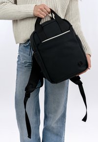 Svart ryggsäck med justerbara remmar och ett texturerat tyg, utrustad med en blixtlåsförsedd framficka och en logotyp i nedre högra hörnet.