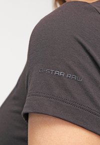 Grå bomullströja med rund hals, med en texturerad tyg och "G-STAR RAW"-loggan broderad på ärmen.