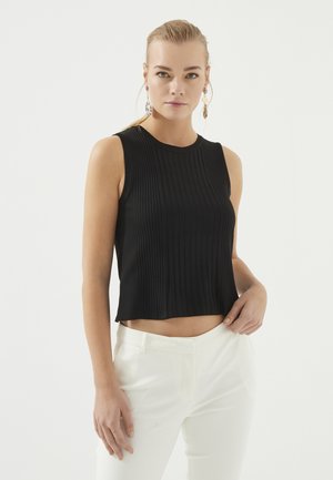 Zwarte geribbelde mouwloze top met een ronde halslijn, in een aansluitend ontwerp en cropped lengte, gecombineerd met witte op maat gemaakte broeken.