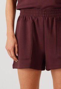 Pantalones cortos deportivos burdeos con cintura elástica, dos bolsillos laterales y una textura suave, que terminan por encima del muslo.