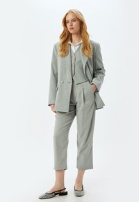 Traje gris claro a medida con chaqueta cruzada, chaleco a juego y pantalones cortos. Un par de zapatos planos adornados completa el look.