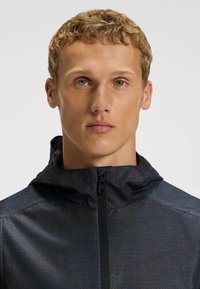 Black hooded jacket with a textured pattern, full zip closure, and a lightweight material, featuring a stand collar and seam details.