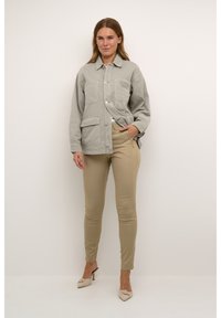 Lichtgrijze button-up jas met twee voork исследovelen, gecombineerd met beige aansluitende broek en beige hoge hakken. Soepele stof, casual ontwerp.