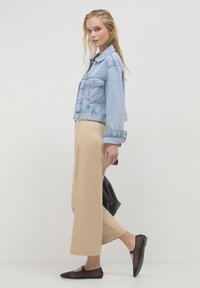 Giubbotto di jeans azzurro chiaro con un design cropped, abbinato a pantaloni beige a gamba larga. Le flat nere con dettagli trasparenti completano il look.