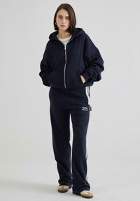 Navy zip-up hoodie med store lommer, parret med matchende sweatpants med sidelommer og et logo-patch, lavet af blødt stof.