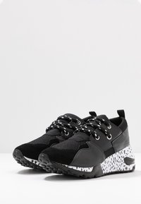 Un paio di sneaker nere con suole a macchie bianche e nere e lacci bianco e nero su uno sfondo bianco.
