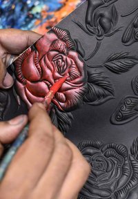 Rood geschilderde rozenrelief op een zwarte textuur, met ingewikkelde details op de bloemblaadjes en bladeren, een penseel vastgehouden in de hand.