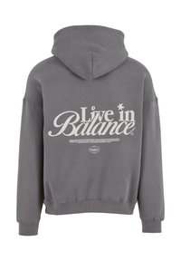 Felpa grigia con cappuccio, con la scritta "Vivi in equilibrio" stampata in bianco sul retro. Presenta una vestibilità comoda e polsini a coste.