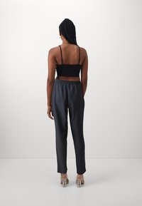 Svart, croppet tanktop med tynne stropper, kombinert med mørkegrå satinbukser med elastisk midje, sett fra baksiden.