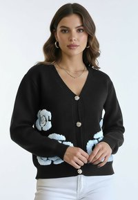 Czarny kardigan z niebieską kwiatową haftem, dekoltem w serek i ozdobnymi guzikami. Miękki dziany materiał i ściągacze na rękawach zapewniają fakturę.