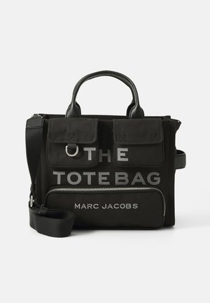 Musta kangaskassi nahkaosilla, jossa on hopeateksti "THE TOTE BAG" ja "MARC JACOBS", kaksinkertaiset kahvat ja irrotettava hihna.