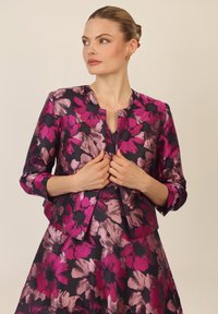 Chaqueta floral en azul marino oscuro con grandes flores rosas y moradas. Presenta un escote redondo y mangas de tres cuartos. Tejido texturizado.