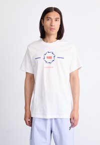 Balta medvilninė marškinė su grafiniu dizainu, kuriame juodu ir raudonu spalvomis užrašyta "NIKE", šalia taip pat yra užrašai "ENGINEERED" ir "SPORTSWEAR".
