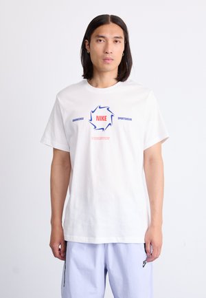 Hvid bomulds-t-shirt med et grafisk design, hvor "NIKE" er trykt i blå og rød, med tilføjelser af teksten "ENGINEERED" og "SPORTSWEAR".