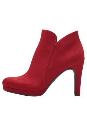 Bottine en daim rouge avec un bout pointu et un talon aiguille haut. Présente une texture lisse et un design épuré et moderne.