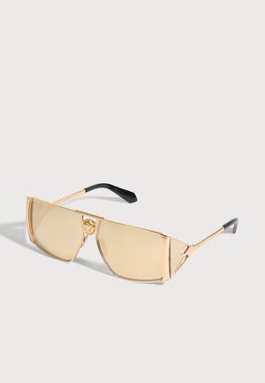 Lunettes de soleil à monture dorée, avec des verres rectangulaires jaune pâle et un emblème circulaire sur le pont, sur fond clair.