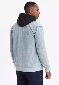 Light blue denim jacket with black hood, ribbed cuffs and hem, relaxed fit, and invisible stitching on shoulders.
