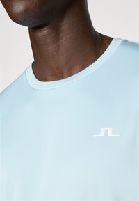 Light blue short-sleeve t-shirt with a crew neck. Features a small white logo on the left chest area and smooth, soft texture.