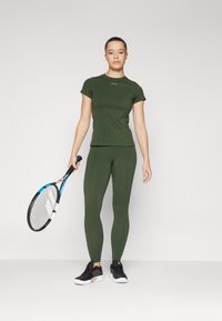 Žalia sportinė marškinė ir kelnių Leggings, pagaminti iš tamprios medžiagos, su aptemptu dizainu. Juodi sportbačiai ir teniso raketė yra įtraukti.