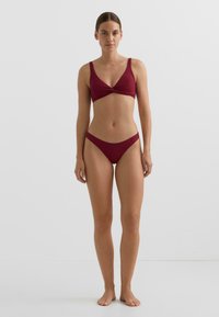 Červená bikini sada v temně červené barvě, s texturovaným žebrovaným vzorem. Podprsenka má nastavitelná ramínka a detail s překroucením vpředu; spodní díl je s vysokým pasem.