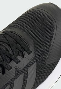 Schwarzer Sportschuh mit Obermaterial aus Mesh, strukturierten schwarzen Akzenten und Schnürverschluss. Verfügt über eine dicke weiße Sohle und dezente Markenkennzeichnung an der Seite.