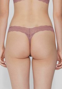 Koronkowy strings w kolorze mauve, z falbaniastym pasem w talii i delikatnym wzorem florystycznym. Miękka tekstura z minimalnym zakryciem.