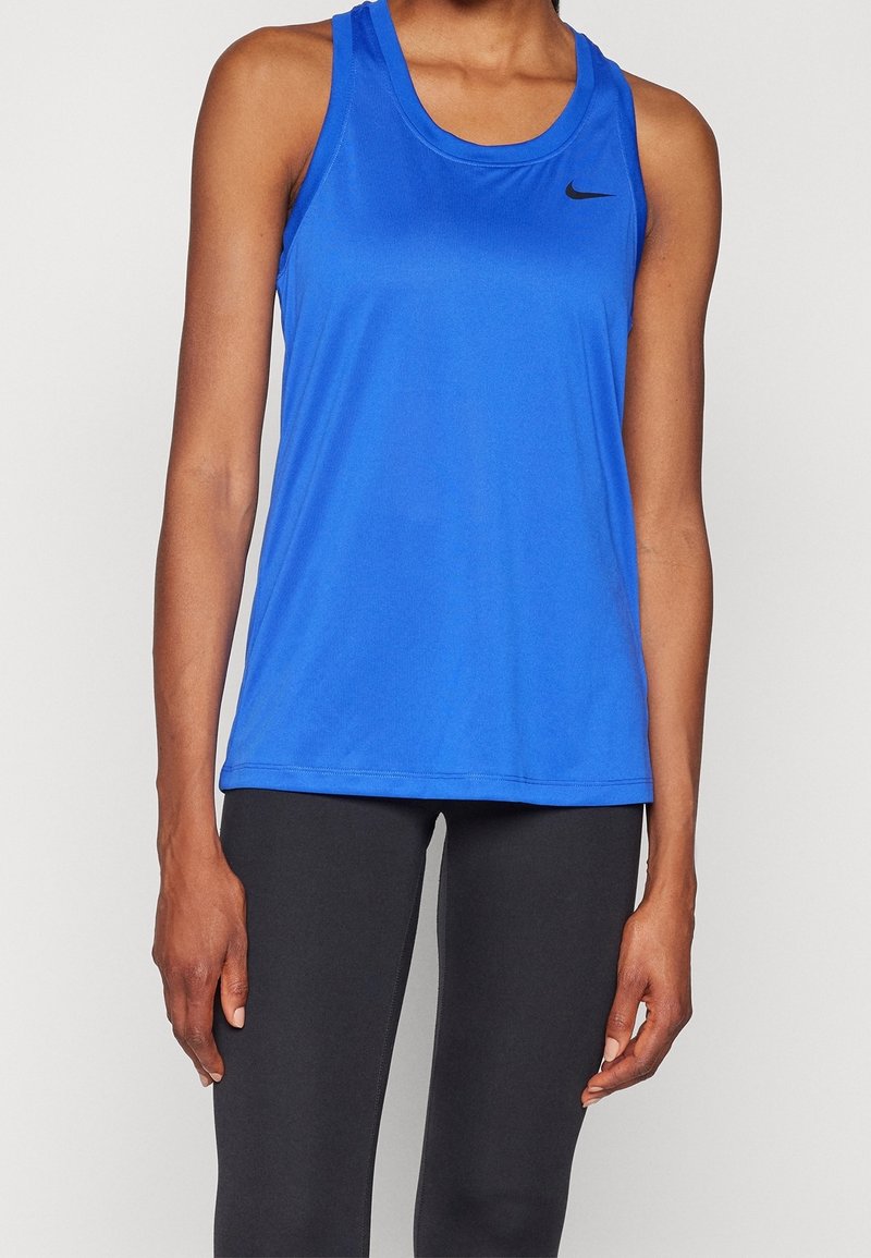 Personne portant un débardeur de sport Nike bleu sans manches et des leggings noirs, debout devant un fond clair uni.