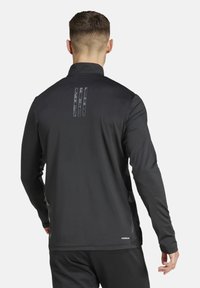 Chaqueta atlética negra de manga larga con cuello alto, rayas reflectantes en la parte posterior y una tela suave y ligera para un mejor rendimiento.