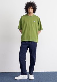 Tricou din bumbac verde cu decolteu rotund și logo alb, asortat cu pantaloni în nuanța navy închis și adidași albi. Detaliu cu cusătură orizontală pe mâneci.