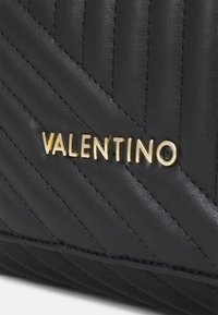 Svart vadderad läderväska med diagonala sömmar och en guld "VALENTINO"-logotyp längst ner. Slät textur med eleganta detaljer.