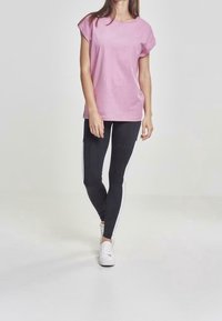 Camiseta de manga corta rosa claro combinada con leggings negros con rayas laterales blancas, complementada con zapatillas blancas. Textura de tejido suave.