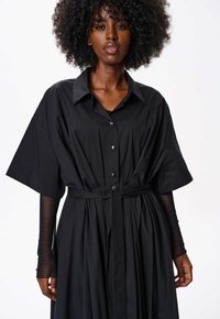 Czarna sukienka z krótkimi rękawami zapinana na guziki, z paskiem w talii i plisowanym dołem. Wykonana z teksturowanej tkaniny, z dużymi guzikami i kołnierzykiem.