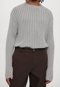 Vaaleanharmaa ribbineuloksinen neulepaita pitkähihainen, pyöreällä kaula-aukkolla ja pehmeällä tuntumalla, yhdistetty tummanruskeisiin korkeavyötäröisiin housuihin.