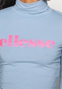 Helles blaues, tailliertes Rollkragenoberteil mit glatter Textur und auffälligem pinkem "ellesse"-Logo auf der Brust. Schlichtes Design, lässiger Stil.