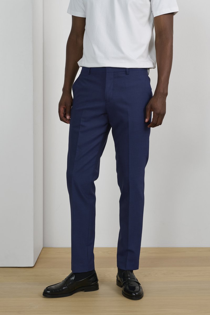 Pantalones ajustados azul marino en un tejido suave, con diseño de pierna recta y bolsillos laterales, combinados con zapatos de vestir negros.