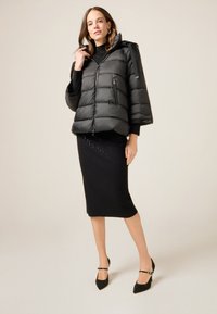 Giacca a vento nera con cappuccio, caratterizzata da un trapuntato orizzontale e tasche con zip. Indossata sopra un vestito nero aderente con delicati embellishments.