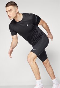 Svart idrottströja med korta ärmar och logotyp på bröstet, tillsammans med svarta shorts. Materialet verkar slätt med en figursydd design.