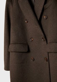 Smeđa vunena dvoredna jakna s velikim gumbima, zakrpanim džepovima i mekanom teksturom. Krojen dizajn sa strukturom siluete.