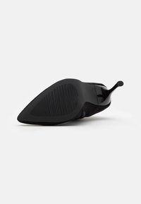 Chaussure à talon haut noire avec un bout pointu, en suède texturé, présentant une semelle noire lisse et un talon fin.