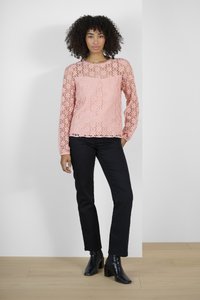 Haut à manches longues en dentelle rose clair avec un motif floral, associé à un pantalon noir à jambes droites et des bottines noires à talons.