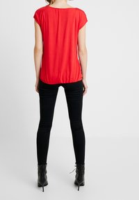 Haut rouge à manches courtes avec un col rond, ourlet froncé, texture lisse, associé à un pantalon noir skinny et des bottines.