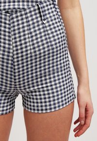 Pantalones cortos con un patrón de cuadros en navy y blanco, de tela de algodón, con un corte ajustado, un bolsillo lateral y un detalle de hardware mínimo.