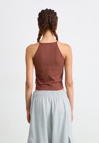 Brun en tettsittende tanktop med spaghetti-stropper, sammen med løse grå joggebukser med elastisk midjebånd og sidelommer.