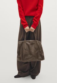 Brown leather tote bag with a textured surface, featuring two elongated handles. The bag has a structured shape and stands out against a neutral background.