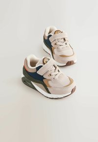Beige and navy sneakers with suede and mesh material, featuring a Velcro strap, textured accents, and a white sole with brown detailing.
