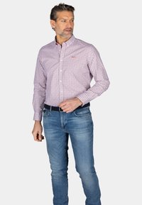  Lichtroze overhemd met een klein geometrisch patroon; gecombineerd met blauwe denim jeans. Heeft een klassieke kraag en lange mouwen.