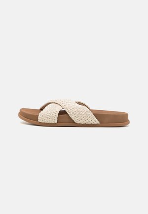 Sandale plate marron avec des brides croisées épaisses en tissu crème tissé et une semelle rembourrée, vue de côté sur fond blanc.