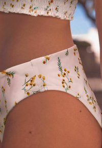 Květinové bikini spodní díl s vysokým pasem, se základní bílou barvou zdobenou žlutými květinami a zelenými listy. Hladká textura a bezešvý design.